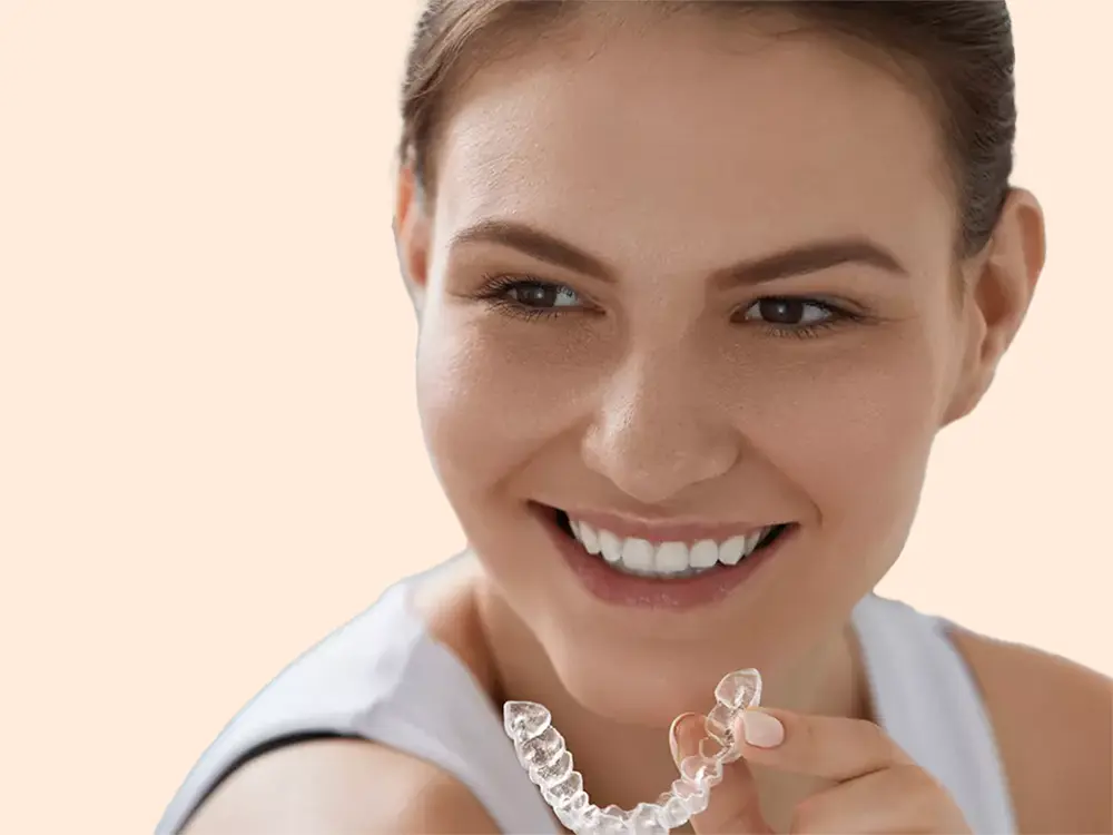Smiling patient holding a clear Invisalign aligner tray near their teeth at P&E Dental.