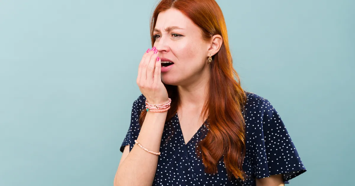 Woman checking her breath while considering possible causes of persistent bad breath
